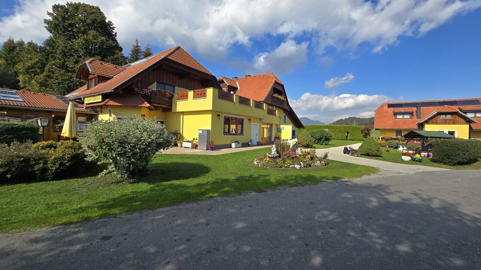 The inviting exterior of the farmhouse, featuring a well-kept garden and a spacious green lawn under a blue sky.