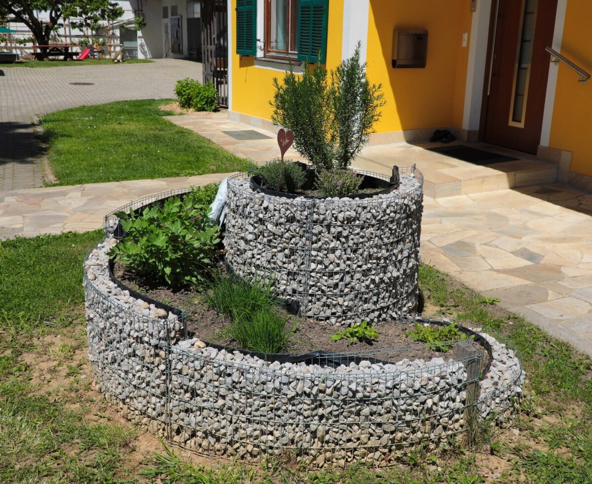 A gabion herb garden with various plants situated by the entrance of the farm house.