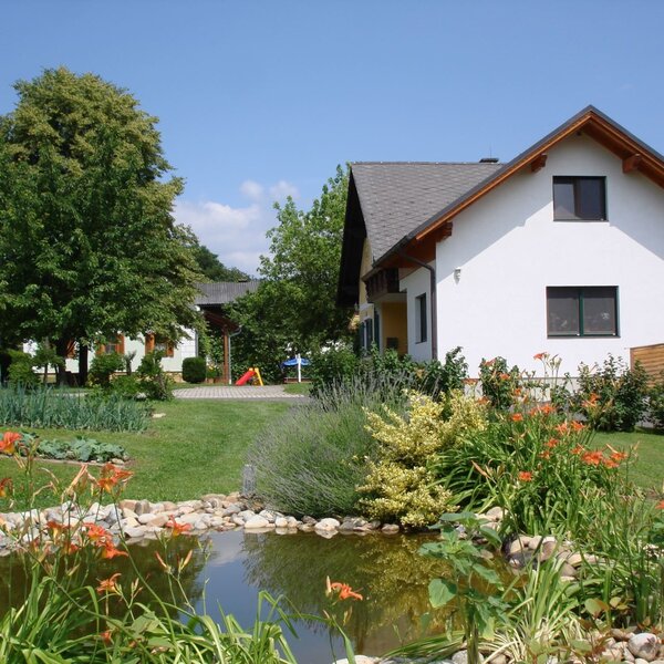 The farm house exterior with a landscaped garden, pond, and visible children's play equipment.