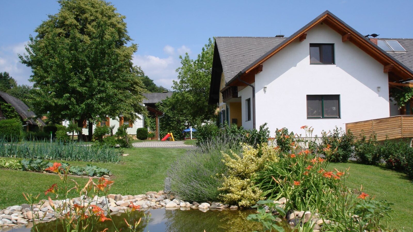 The farm house exterior with a landscaped garden, pond, and visible children's play equipment.