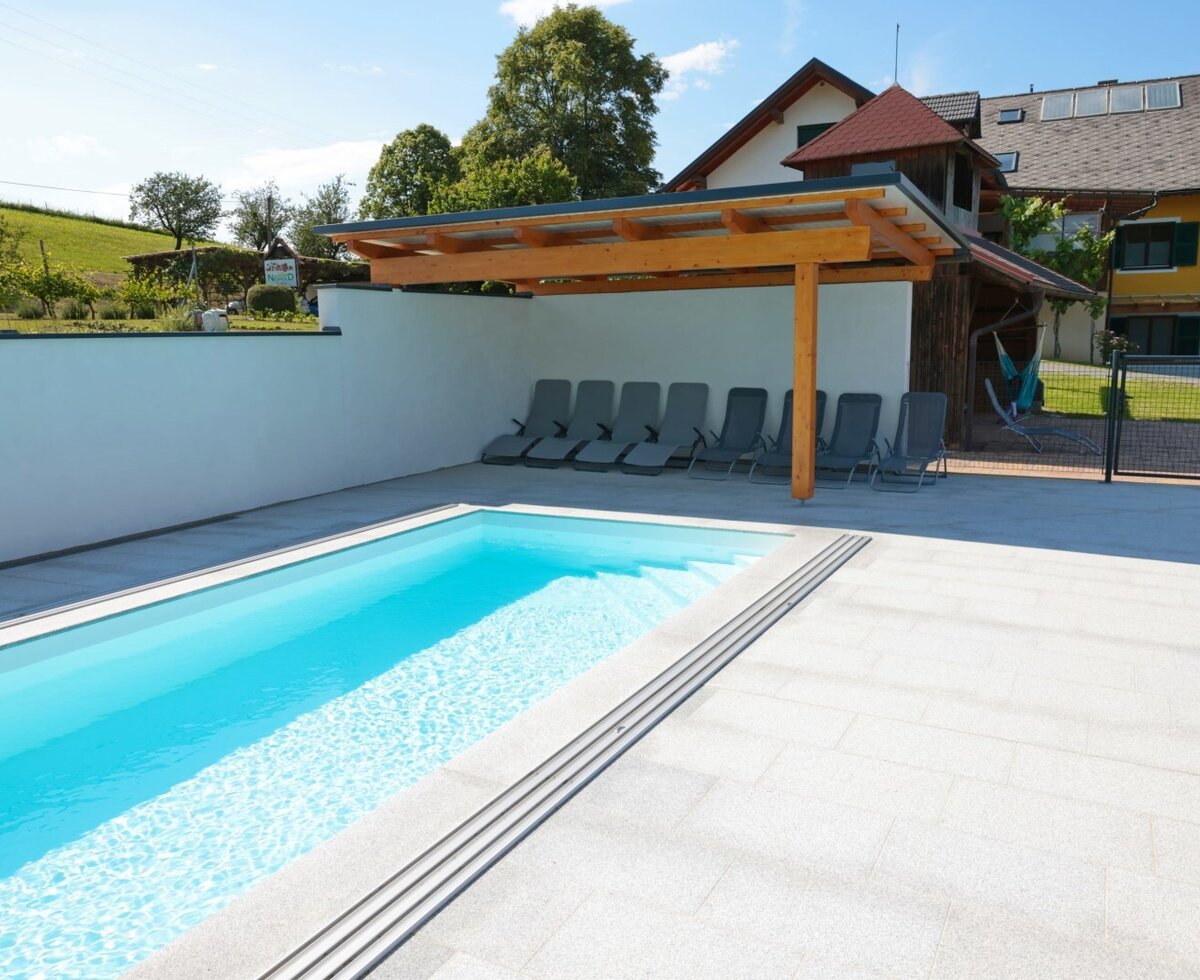 The farm house's outdoor swimming pool features a paved surround, sun loungers under a wooden pergola, and a visible portion of the main building.