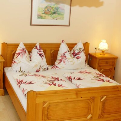 A bedroom in the Farm House features a wooden double bed with patterned bedding, two wooden nightstands, and individual lamps.