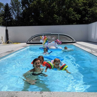 The outdoor swimming pool at the Farm House, with a retractable cover, an outdoor shower, and guests in the water.