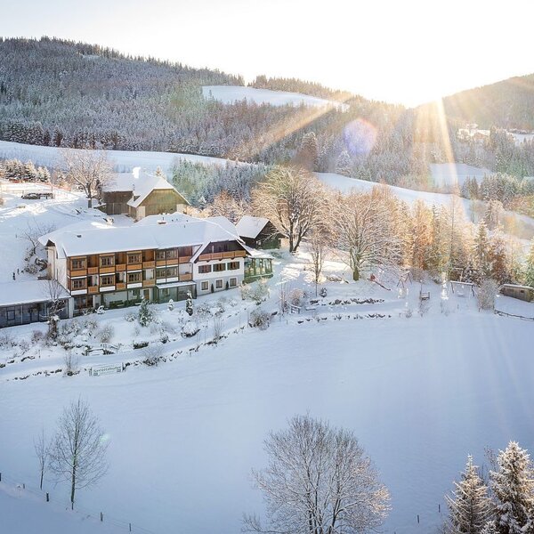 The Farm House set in a snow-covered winter landscape with surrounding hills and sunbeams.