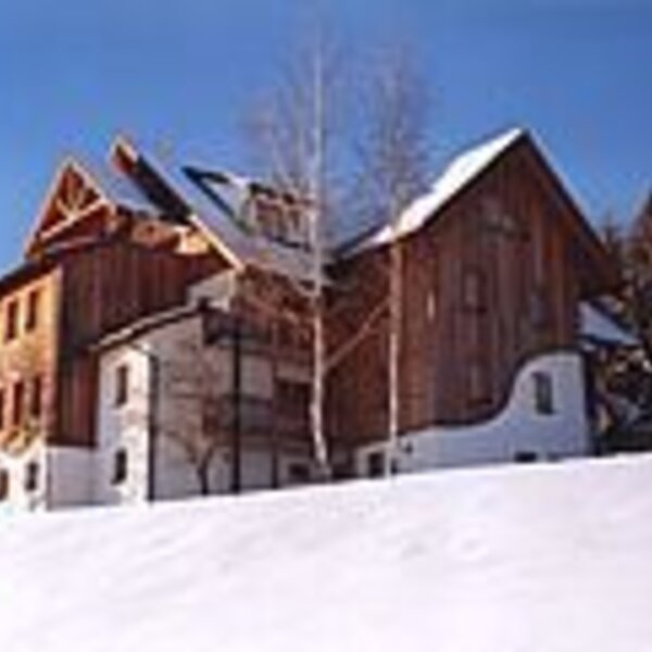 Exterior view of the farmhouse in the snow with a wooden facade and white base.