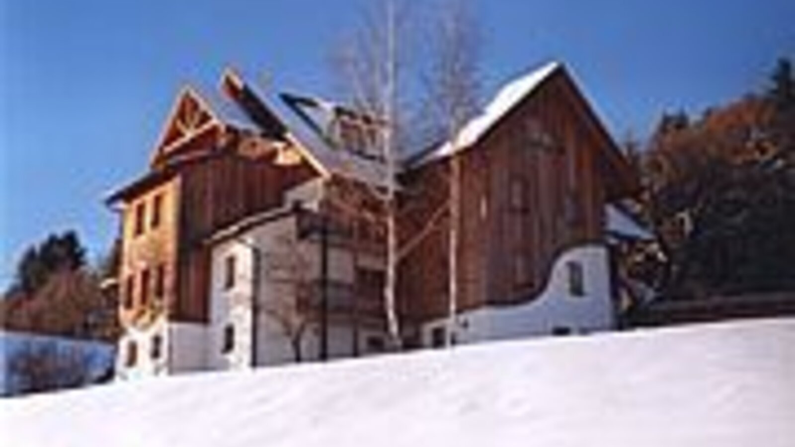 Exterior view of the farmhouse in the snow with a wooden facade and white base.
