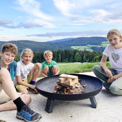Children gathered around a fire pit at the farmhouse, with a view of the mountains.