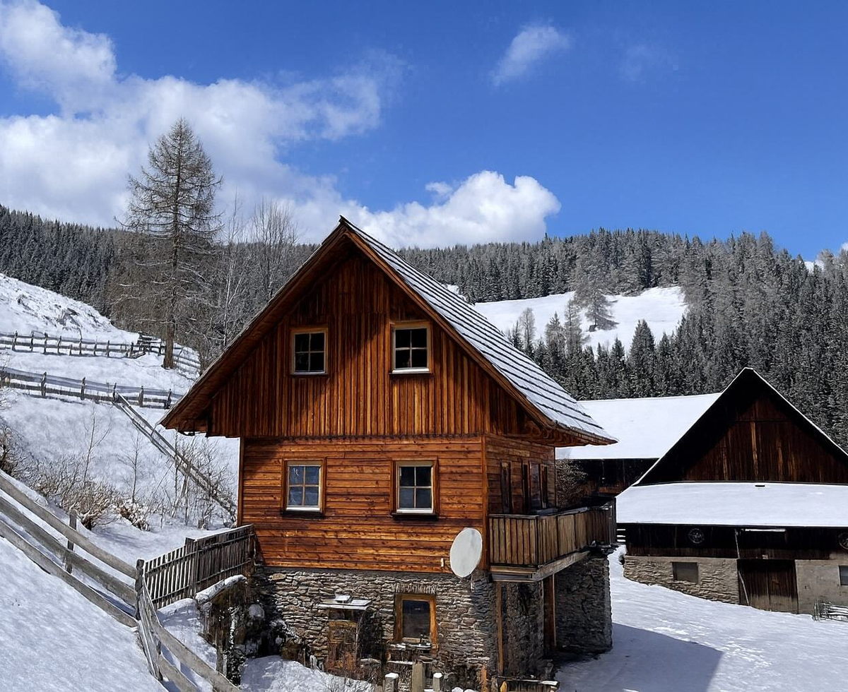 The Bed and Breakfast building with a wooden facade, stone foundation, and balcony in a snowy mountain landscape.