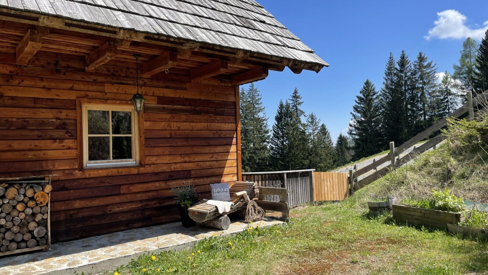 Exterior view of the Alm, featuring a wooden facade, window, woodpile, and a log bench.