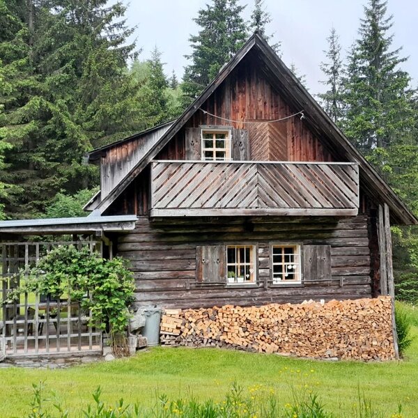 Exterior view of the Bed and Breakfast, a wooden house with a balcony and covered seating area, surrounded by forest.