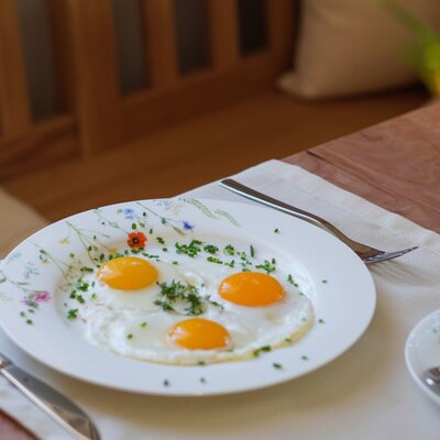 Breakfast served at the Farm House, featuring a plate of fried eggs with chives, cutlery, and a teacup on a wooden table.