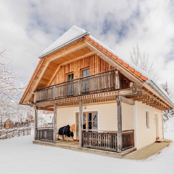 The Farm House exterior featuring a wooden upper-level balcony and a ground-floor covered porch, surrounded by snow.