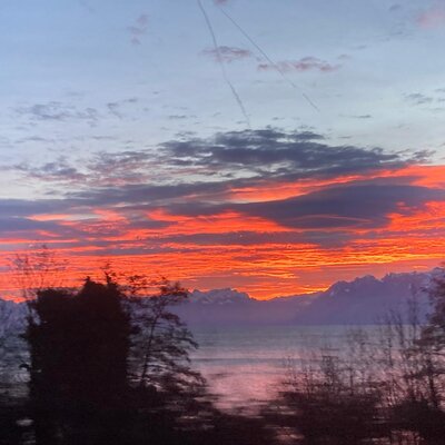 View from the Farm House at sunset, featuring a lake, mountains, and red and orange skies.