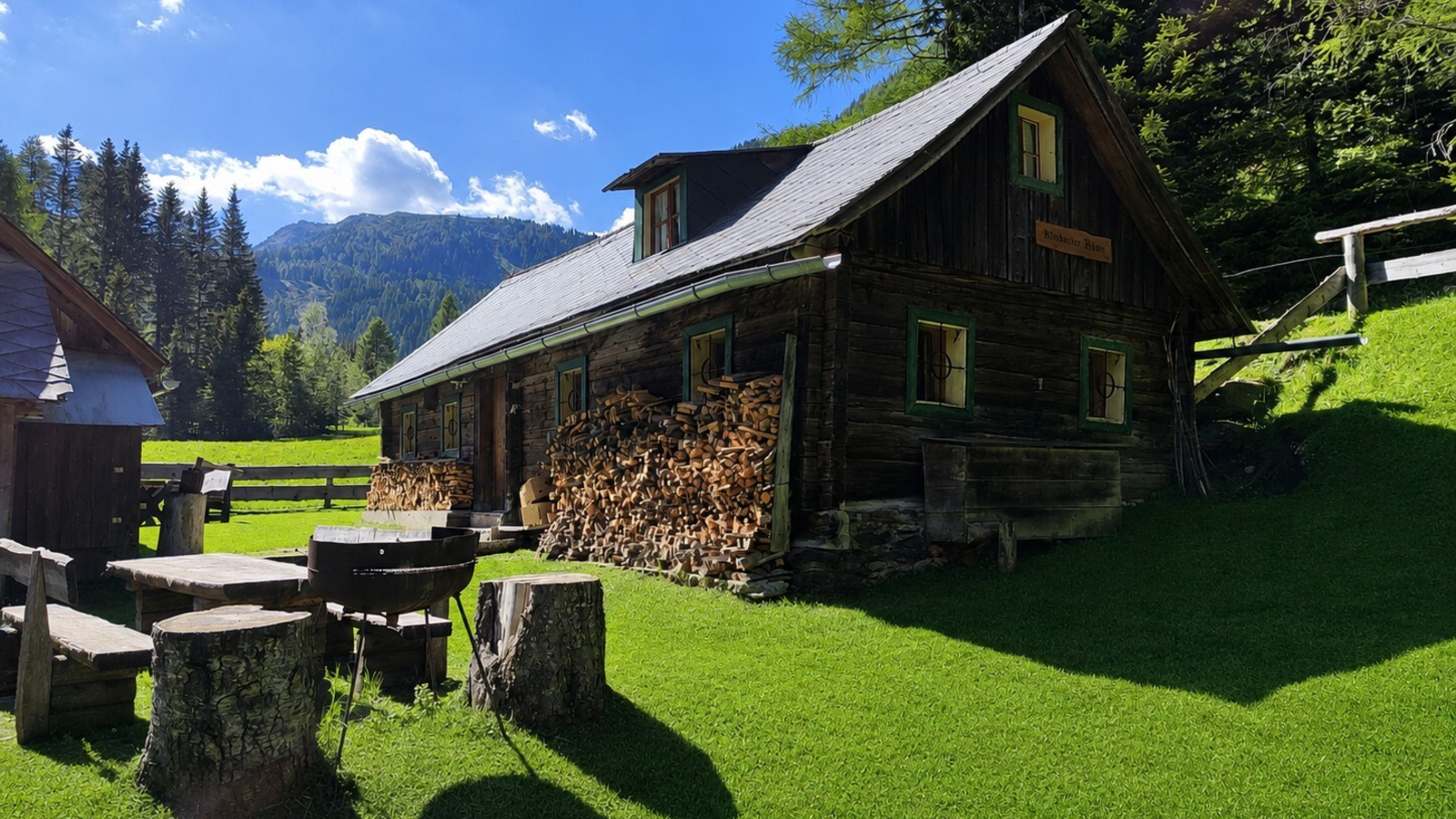 The bed and breakfast's rustic wooden cabin set in a sunny meadow with cozy outdoor seating and mountain views.