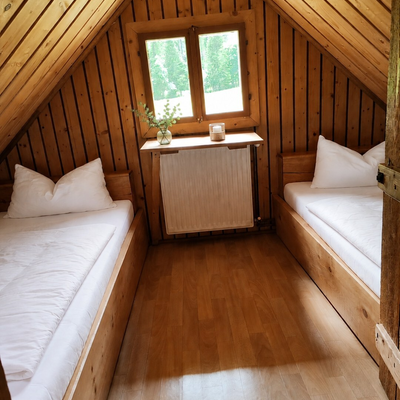 A cozy bedroom in the bed and breakfast featuring wood-paneled sloped ceilings, two single beds, and a small window.