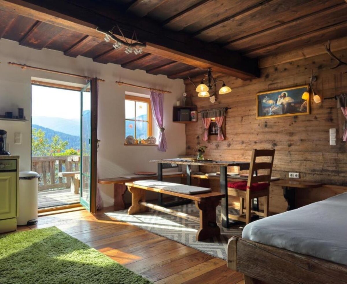 The cozy dining and living area of the Ottls Hütte, featuring rustic wooden walls, traditional seating, and direct access to a sunny balcony with mountain views.