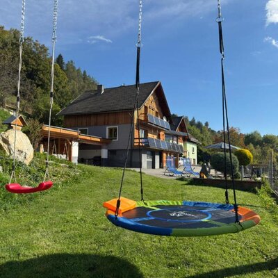 The inviting garden featuring a lush green lawn and colorful swings against a scenic hillside backdrop.