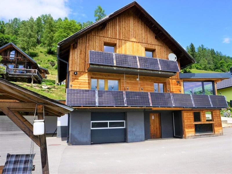 The inviting woodenWind Buam Hütte featuring sunny balconies with solar panels, set against a green hillside.