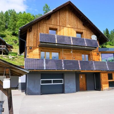 The inviting woodenWind Buam Hütte featuring sunny balconies with solar panels, set against a green hillside.