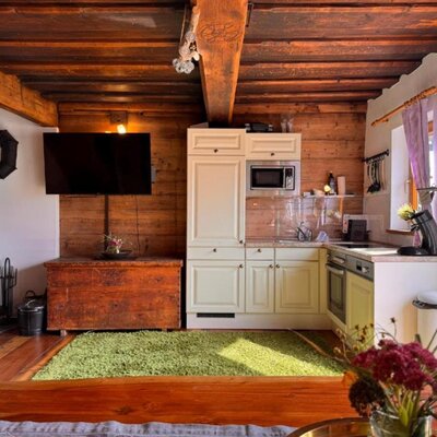 The cozy living area in the Ottls Hütte, featuring a well-equipped kitchenette, a wood-burning stove, and rustic wooden beams.
