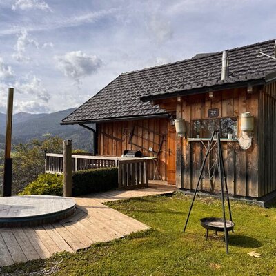 A rustic wooden holiday home featuring an inviting deck with a hot tub and an outdoor fire pit against a scenic mountain backdrop.
