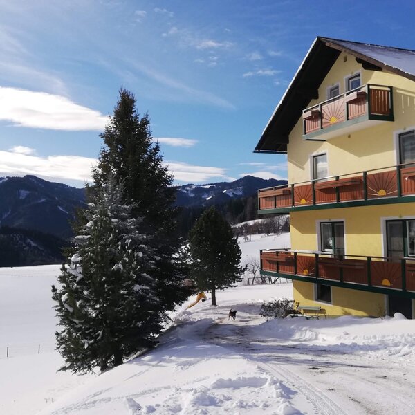 The Farm House features a yellow exterior with multiple balconies, set against a snowy landscape and distant mountains.