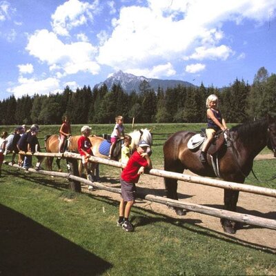 Horse riding activity for children at the Farm House, with multiple horses and a mountain backdrop.