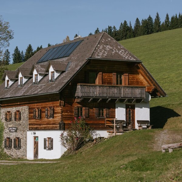 Exterior view of the farmhouse, featuring a wood and stone facade, a balcony, and solar panels on the roof.