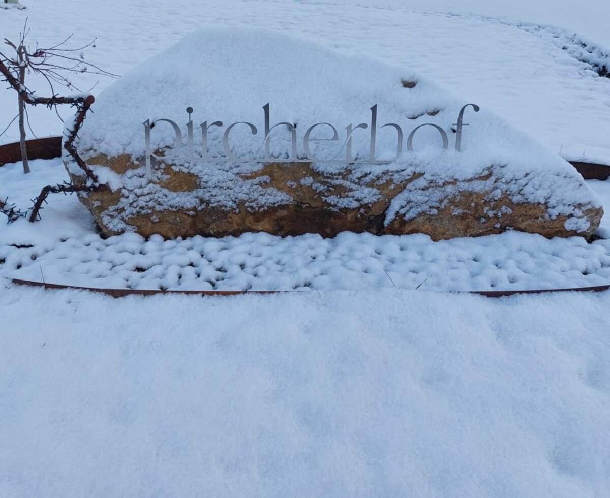 The entrance sign for the Farm House, featuring "pircherhof" lettering on a stone, is surrounded by snow and a star decoration.