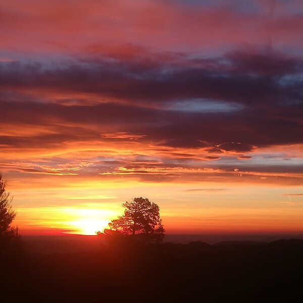 The farmhouse offers views of colorful sunsets over silhouetted trees and distant hills.