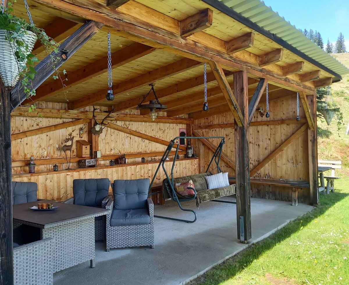 The farmhouse offers a covered wooden outdoor area equipped with a dining set and a swing bench.
