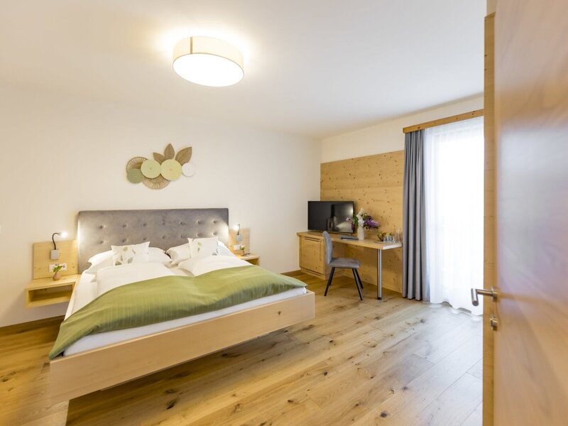 Double bedroom in the farmhouse with a large bed, wooden floor, desk, television, and balcony access.