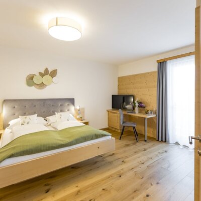 Double bedroom in the farmhouse with a large bed, wooden floor, desk, television, and balcony access.