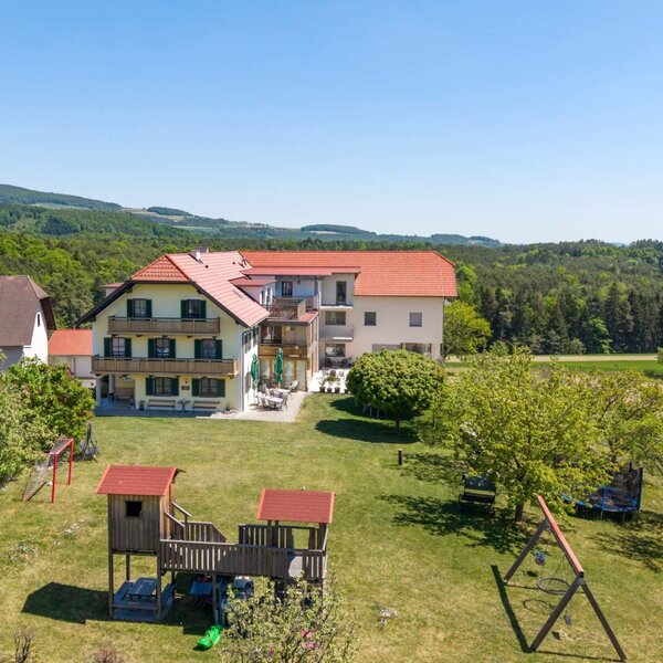 The farmhouse with balconies and an outdoor terrace, surrounded by a garden with a children's playground and the landscape of Pöllauer Tal.