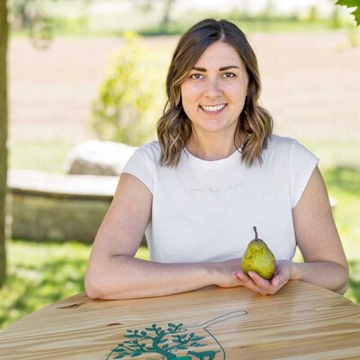 The hostess of the farmhouse presents a Hirschbirne pear at a wooden table featuring the farmhouse's logo.