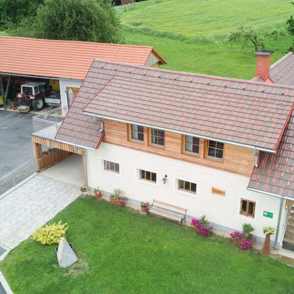 The Farm House exterior with a red tiled roof, a green lawn, a paved driveway, and an adjacent farm building with machinery.