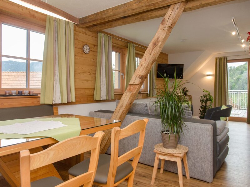 The Farm House features a combined living and dining area with wooden furnishings, a sofa, flat-screen TV, and balcony access overlooking mountains and trees.