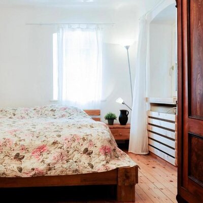 Farmhouse bedroom with a wooden bed, floral bedspread, bedside table, and a large wooden wardrobe.