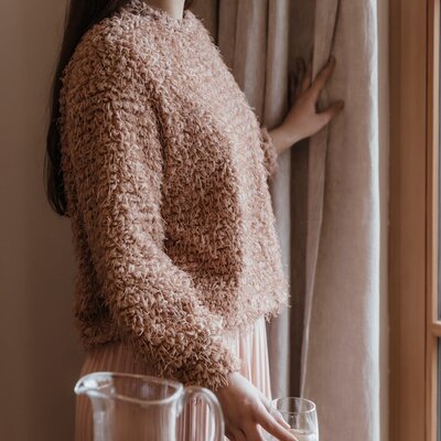 A guest standing by a window in the Farm House, next to a wooden table with a pitcher of water.
