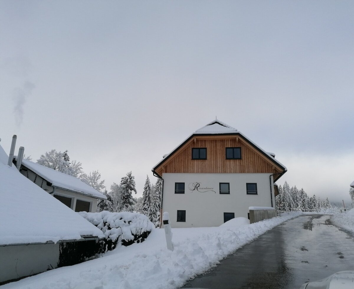 The Farm House exterior with a white facade and wooden upper gables, featuring a snow-covered roof and a cleared paved driveway in winter.
