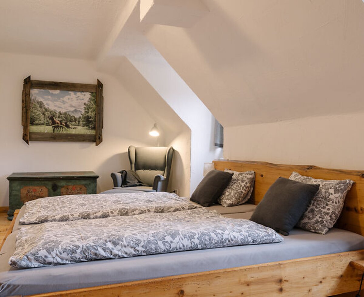 Bedroom in the farmhouse featuring a double bed, sloped ceiling, and reading armchair.