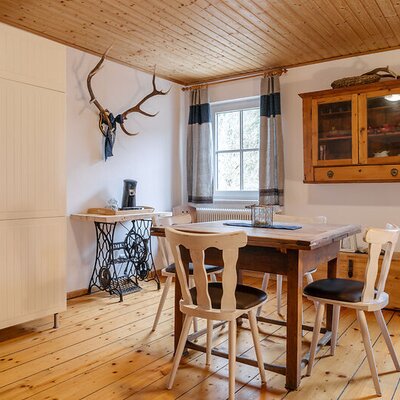 Dining area in the farmhouse featuring a wooden table for meals, chairs, and a partially visible kitchen unit.