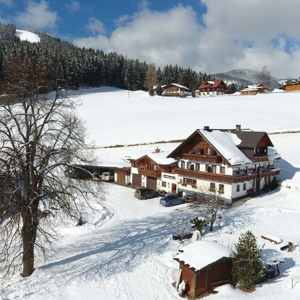 The Farm House complex features traditional buildings with balconies and snow-covered roofs, situated in a winter landscape surrounded by snowy fields and pine forests.