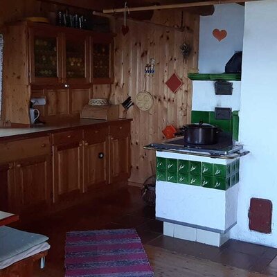 The farmhouse features a combined wooden kitchen and dining area, a traditional tiled stove, and a single bed.