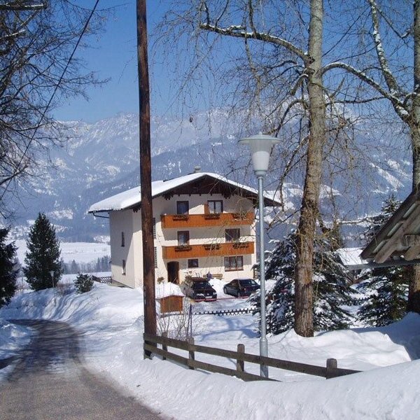 The farm house with balconies, situated in a snowy, mountainous landscape with an access road.