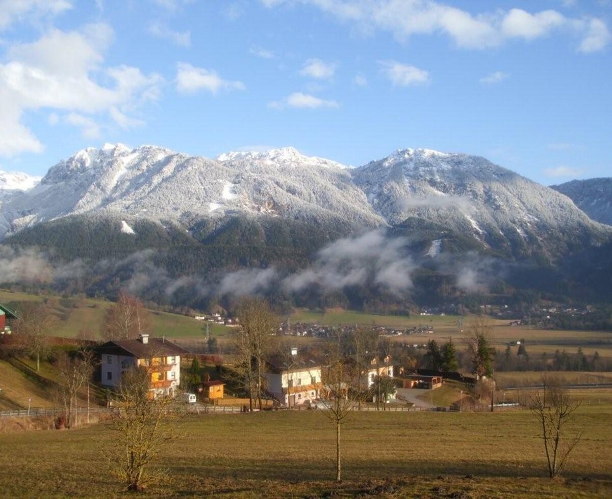 The landscape surrounding the Farm House, featuring snow-capped mountains and a valley with fields and a village.