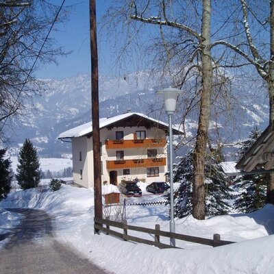 The Farm House exterior in winter, featuring balconies and a snowy mountain backdrop.