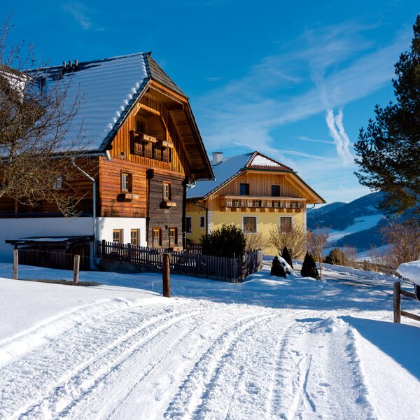 The farmhouse exterior with traditional wooden elements and snow-covered roofs, set amidst a winter landscape with distant mountains.