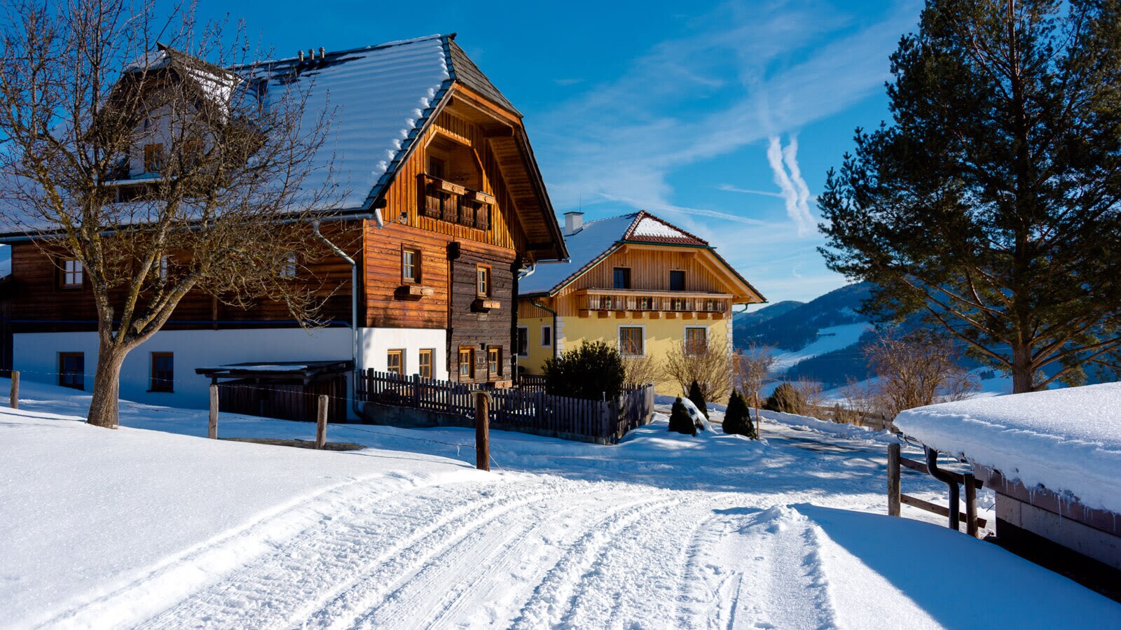 The farmhouse exterior with traditional wooden elements and snow-covered roofs, set amidst a winter landscape with distant mountains.