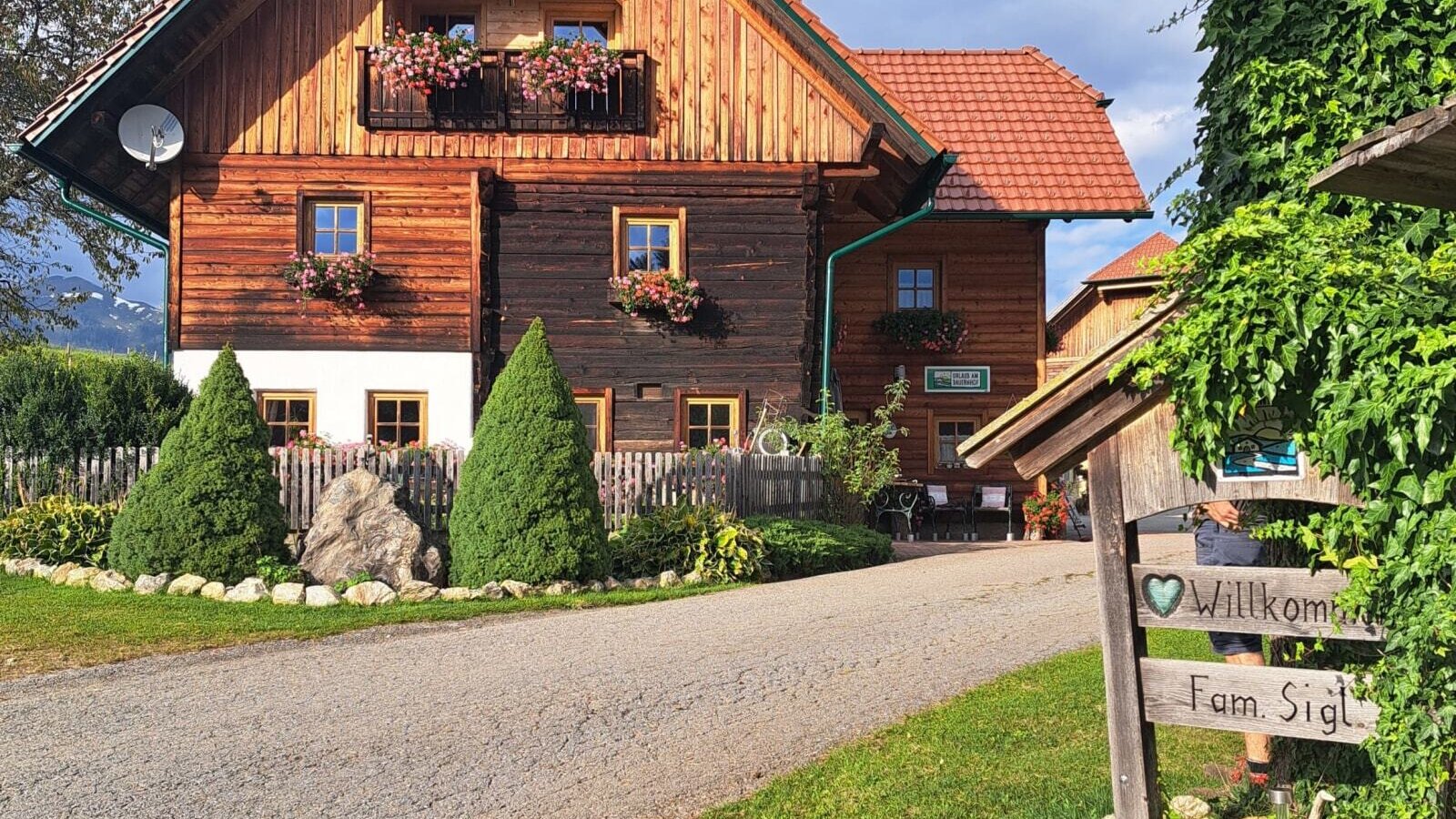The exterior of the farmhouse, featuring a wooden balcony with flower boxes and a welcome sign at the entrance.